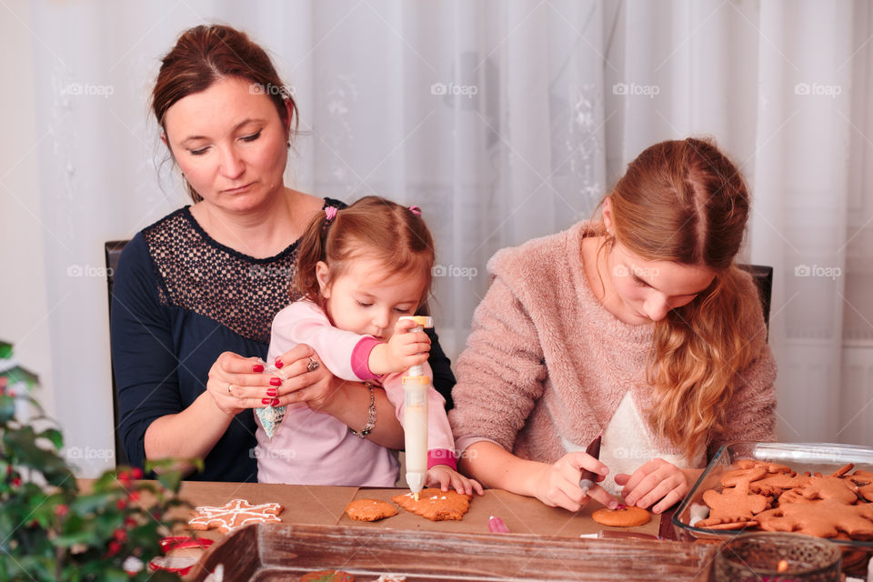 Family decorating baked Christmas gingerbread cookies with frosting