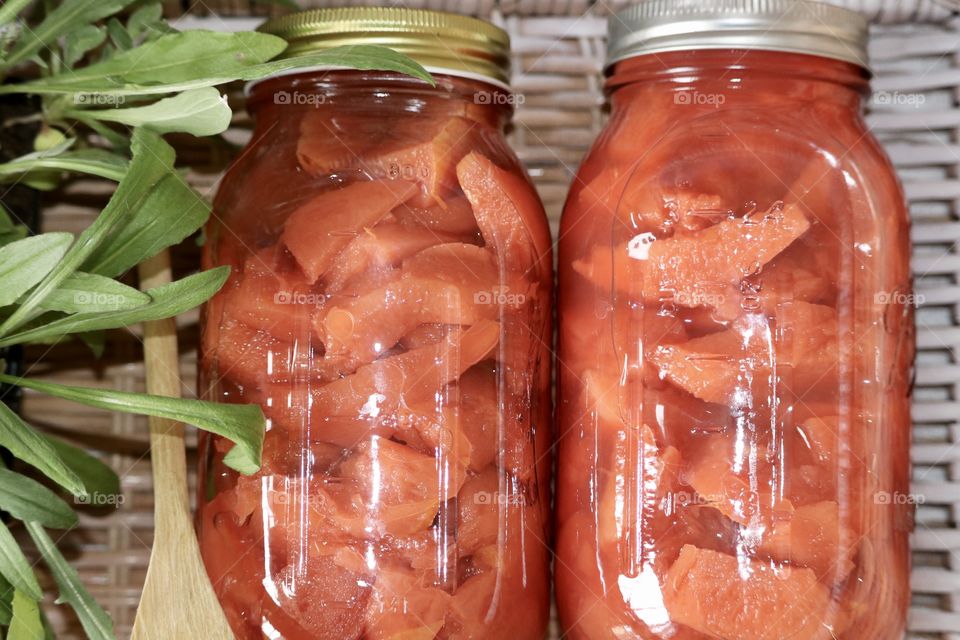 Transformed from yellow to rosy colour, the more quince fruit is cooked the darker red it becomes. Two quart sized glass canning jars flat lay in wicker basket with fruit