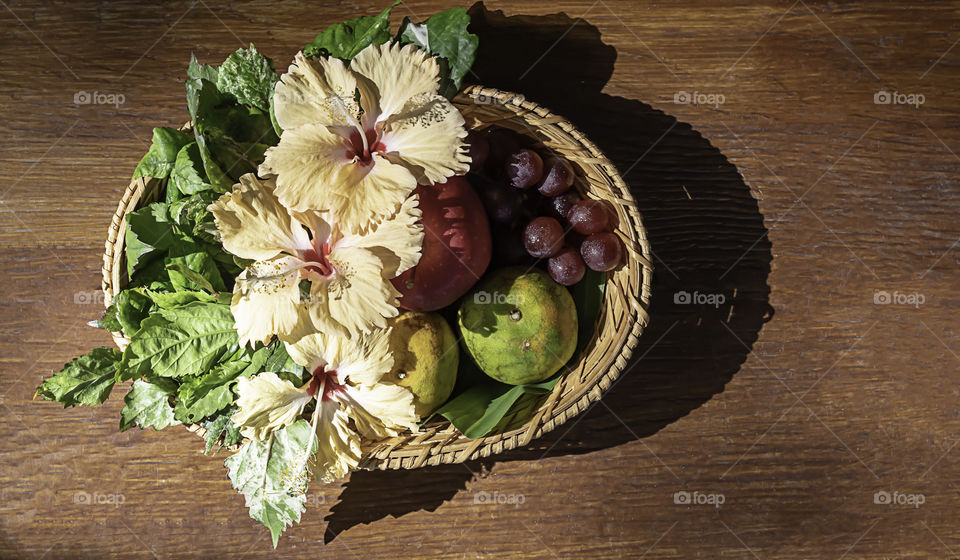 Apple, Orange and grape in weave bamboo baskets with floral decorations on wooden table.