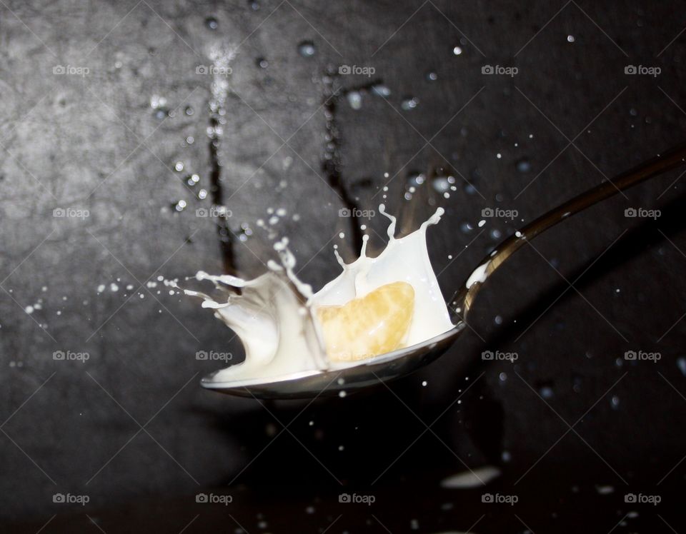 It is a slice of tangerine that falls into a spoon full of milk. The photograph is made closely so that both the drops of milk and the milk and the tangerine slice can be appreciated well.