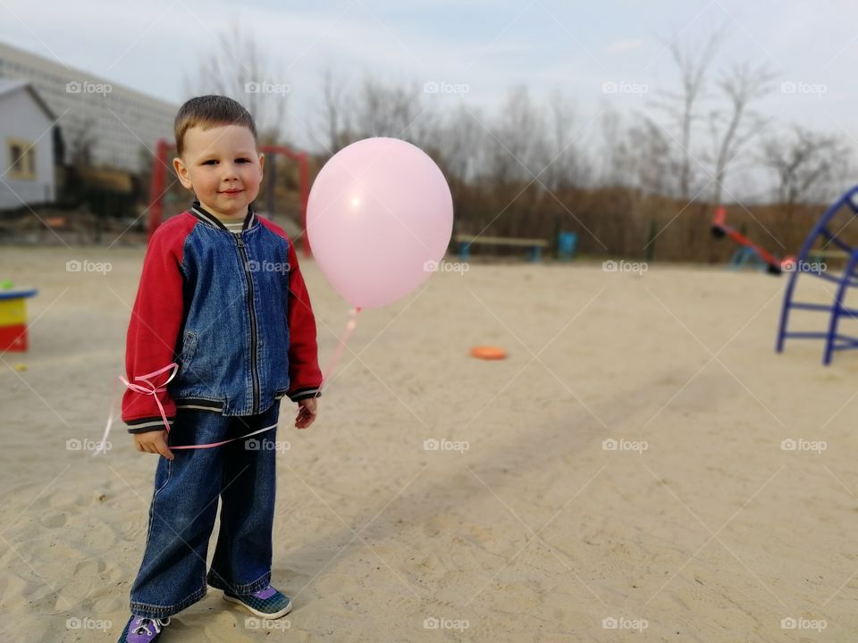 The boy holds a pink balloon