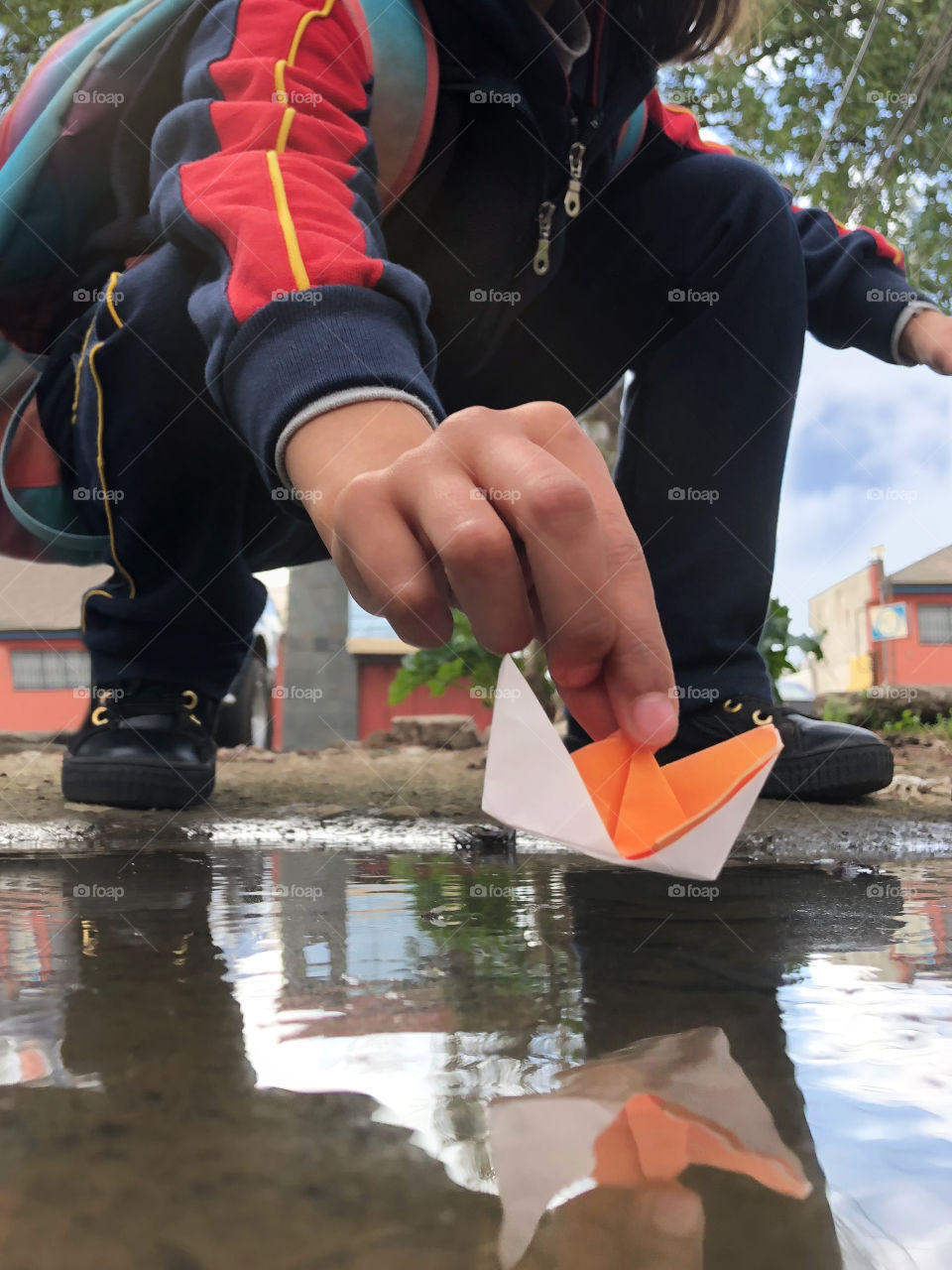 little girl putting origami boat in a puddle of water