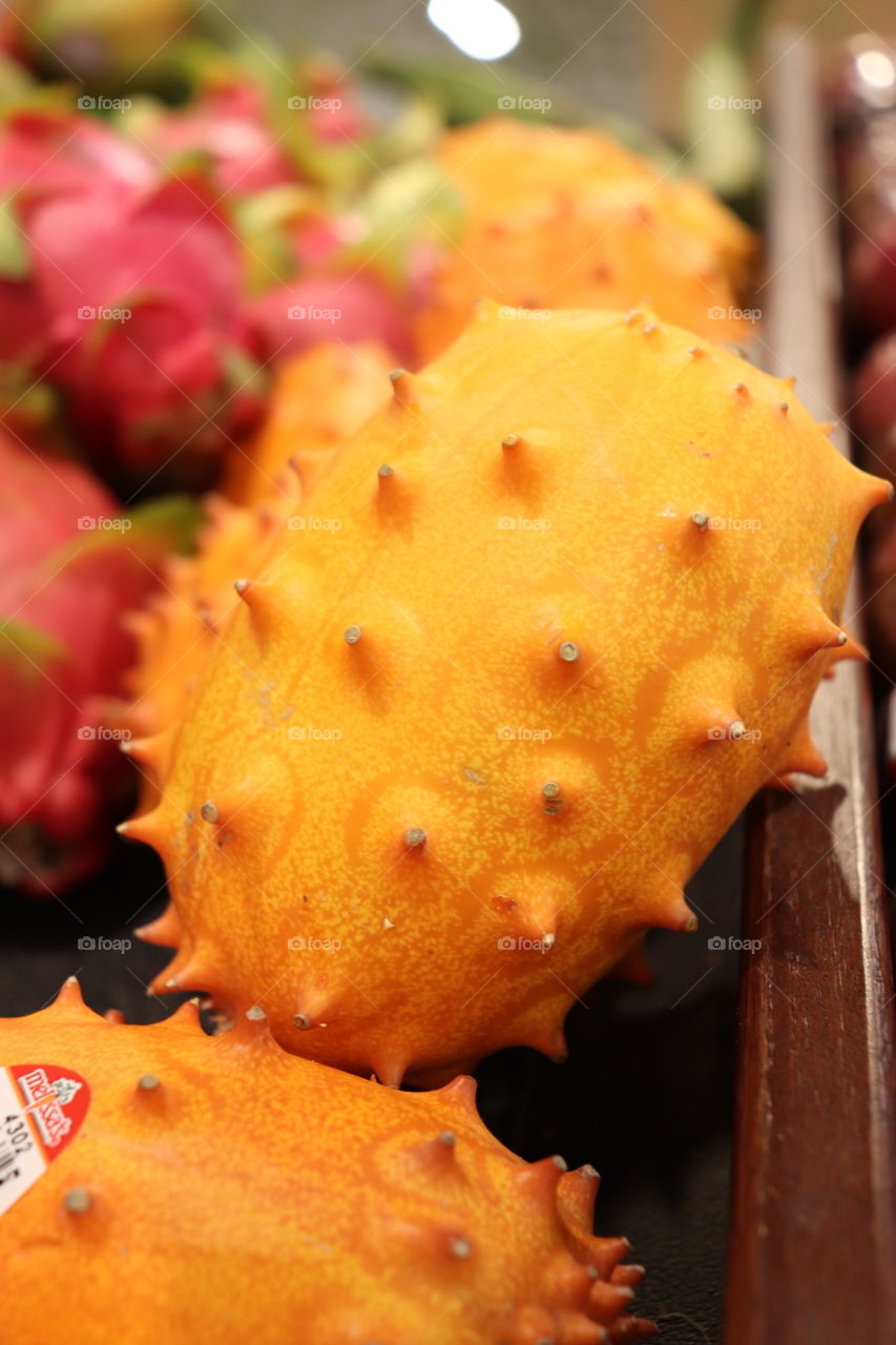 Bright orange, spiky melon, with dragonfruit on the side. This fruit is known as a Kiwano melon. 