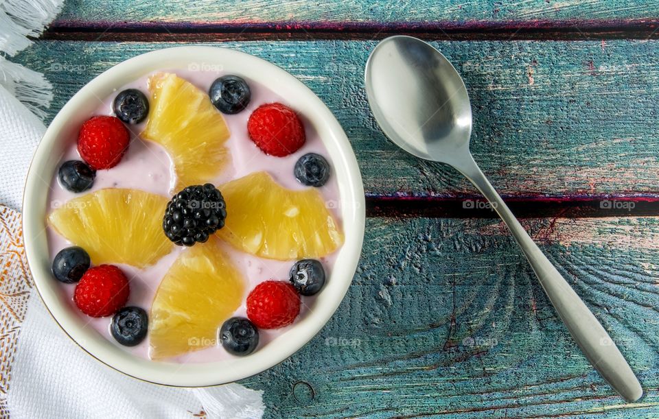 Yoghurt, banana and strawberry smoothie topped with pineapple, raspberries, blueberries and blackberry