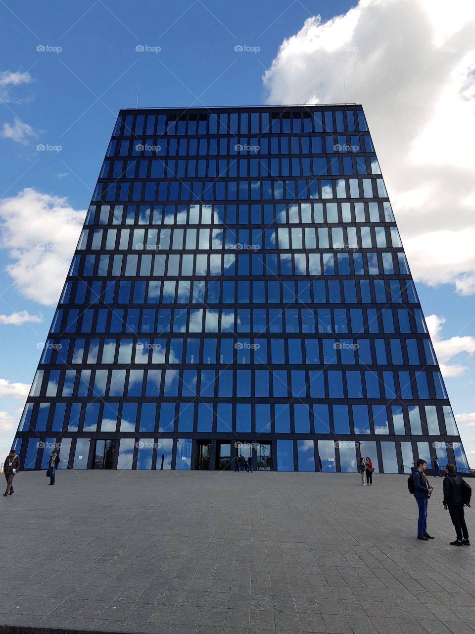 Minimalistic modern glass building reflects clouds in the bright sky.