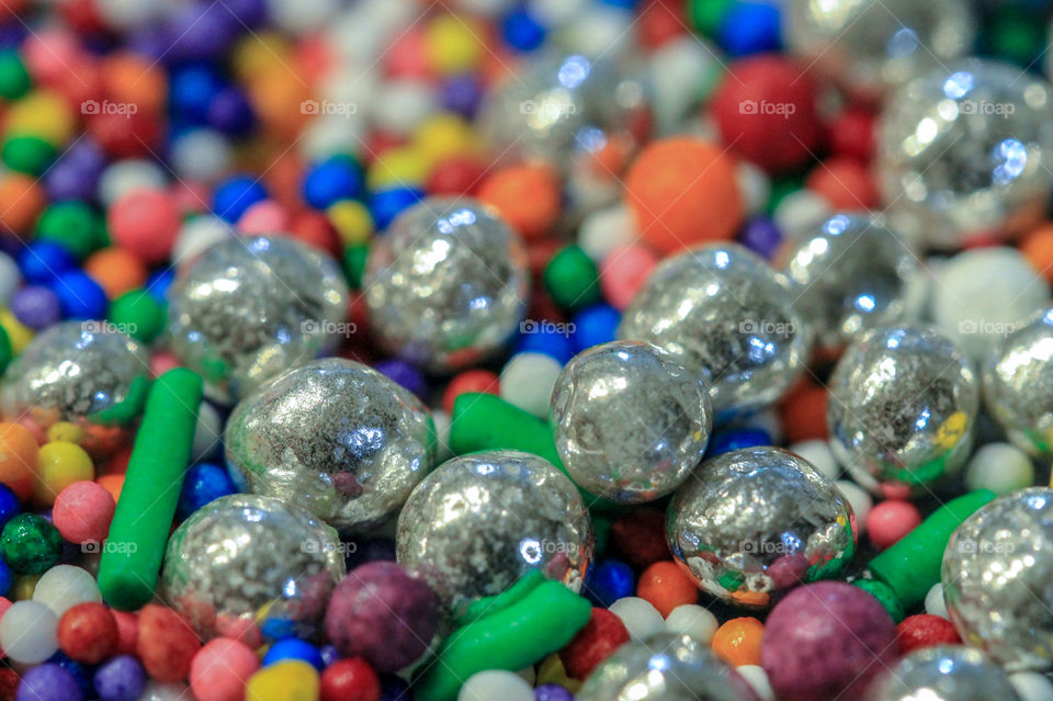 Macro of multi-coloured candy sprinkles of different sizes & shapes. There are also silver balls, dragees, reflecting the other candies & the room. 