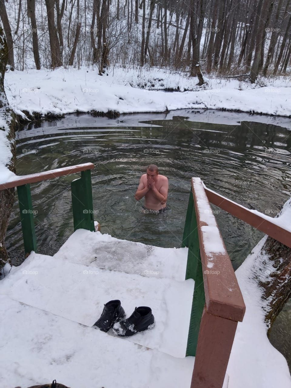 A man bathes in a lake in winter against the backdrop of forest and snow in the cold
