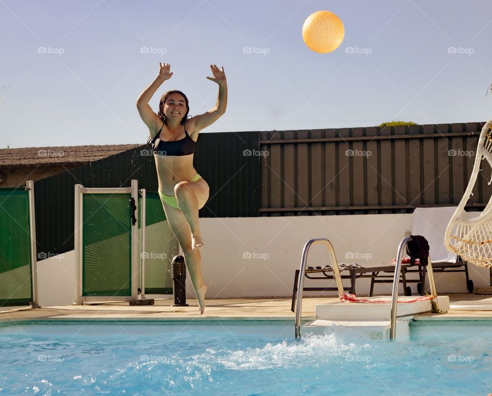 Young woman jumps for the ball into the swimming pool