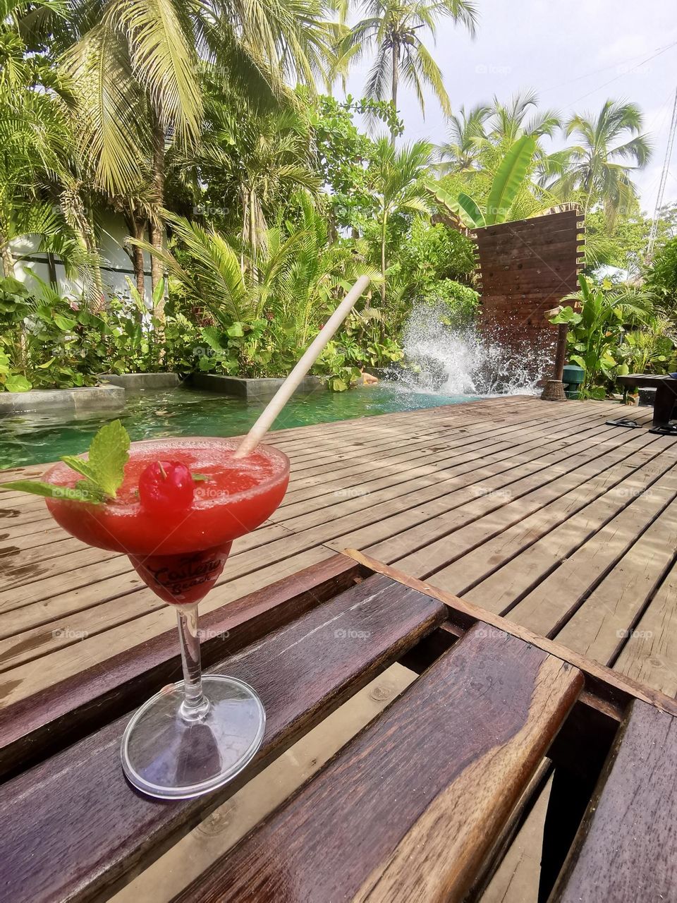 A pool with wood floor and a tasty cocktail 