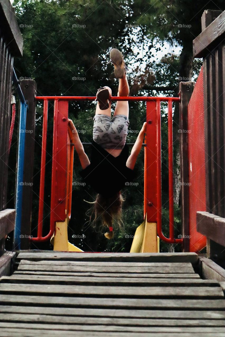 Girl on the top of a slide rolling with her head down 