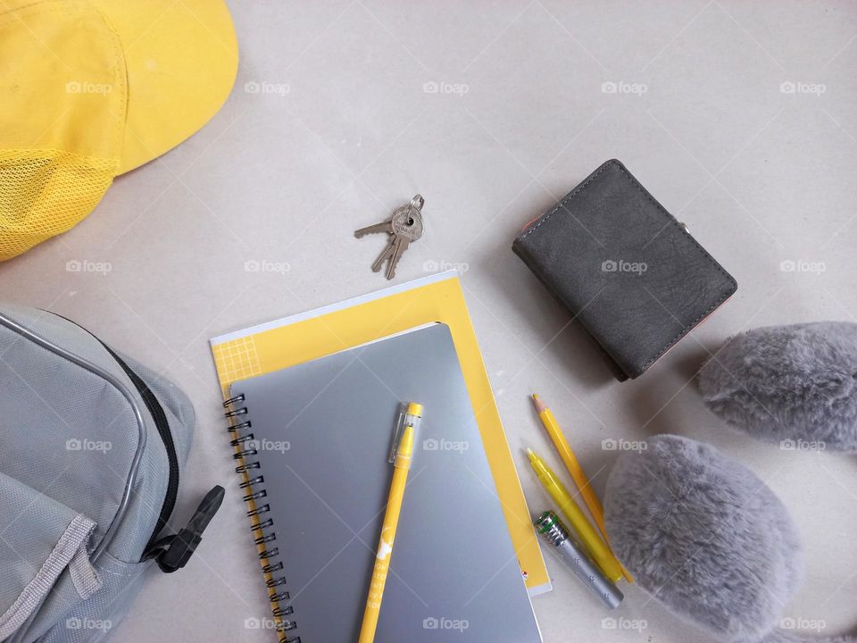 items and accessories in yellow-gray colors, a gray bag, a gray wallet, a gray notebook and a yellow cap, a yellow notebook, a pen, a pencil,gray headphones.