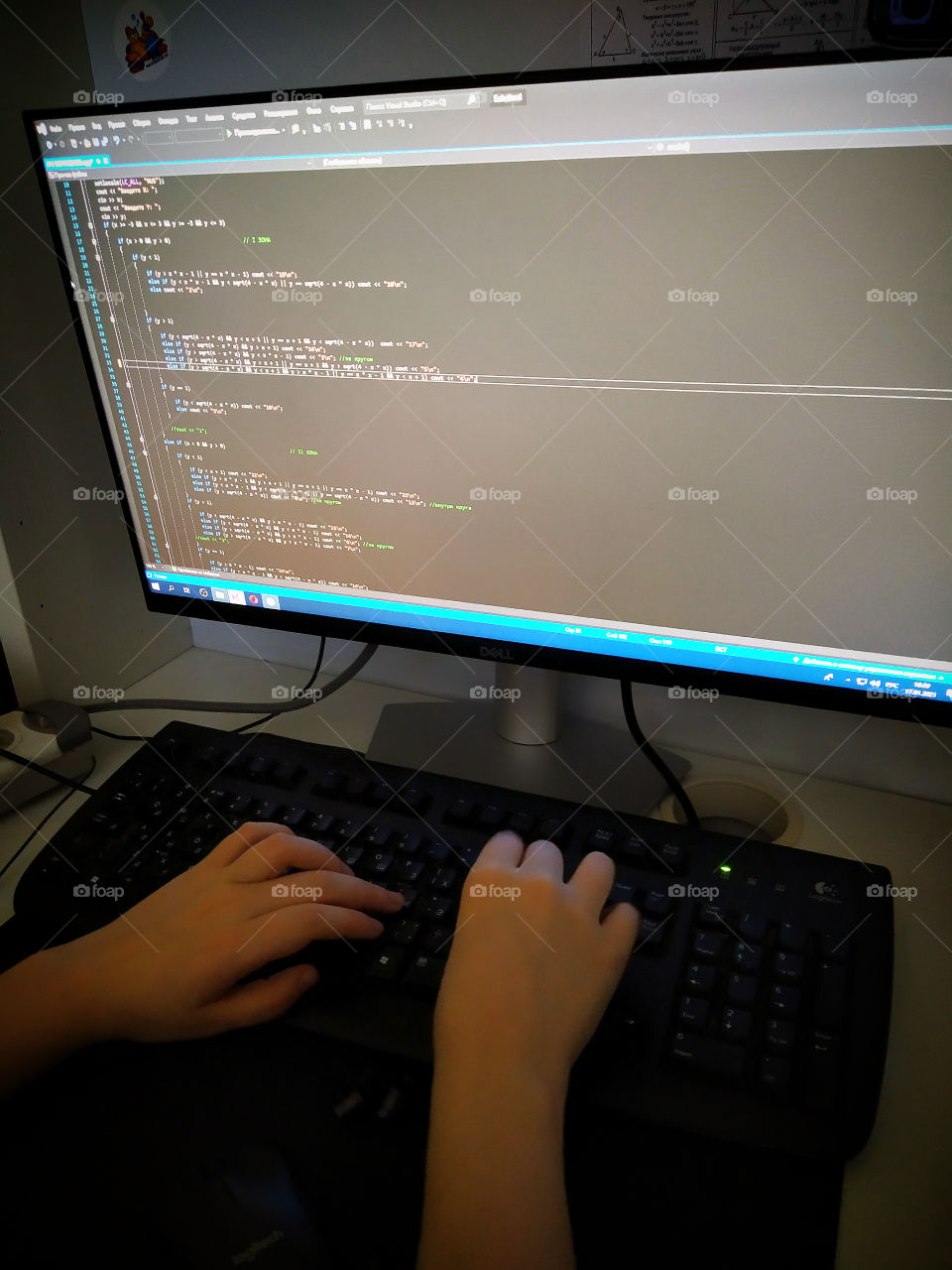 Hands behind the keyboard on the background of the monitor with the program.  The programmer writes the program
