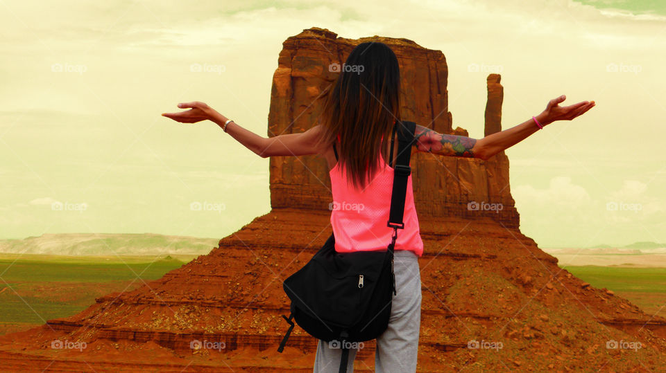 A woman with open arms is looking at the big monolith that is in the famous Monument valley tribal park