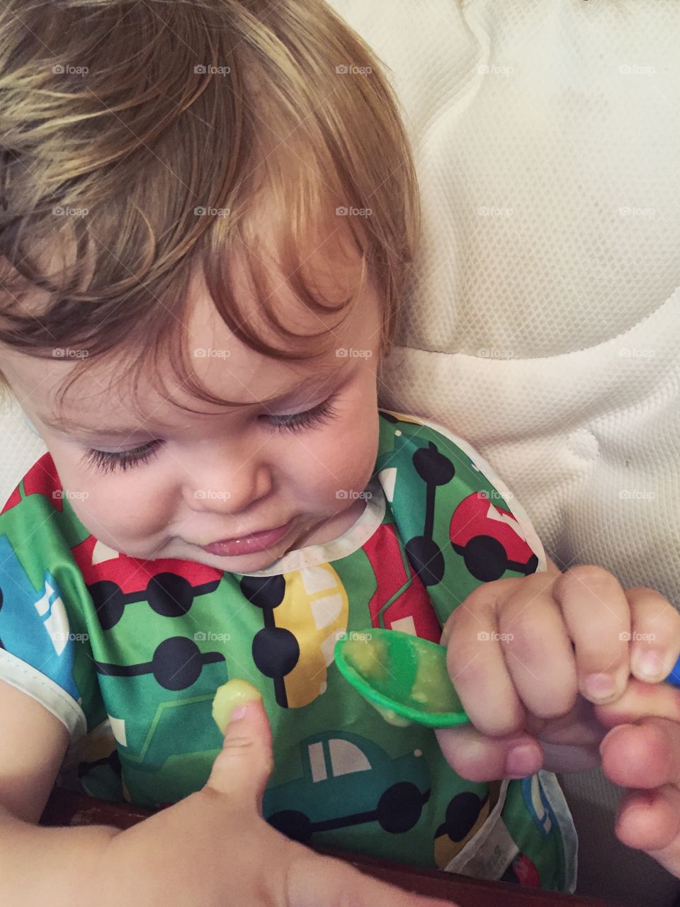 Cute toddler holding spoon with cream on thumb