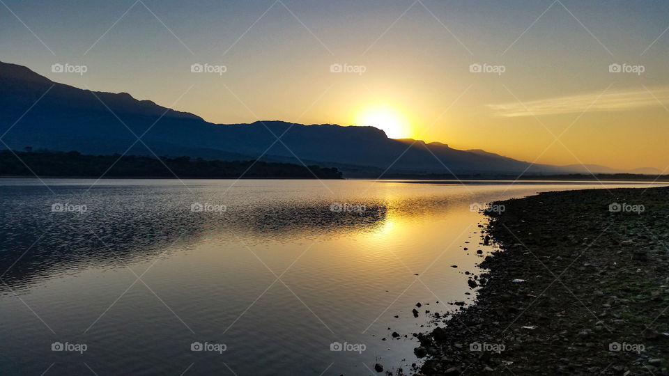 sun setting behind a mountain with reflection on the water