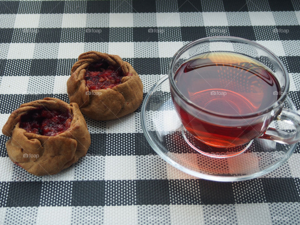 There is a cup of tea and two pies with fruit filling on the table.