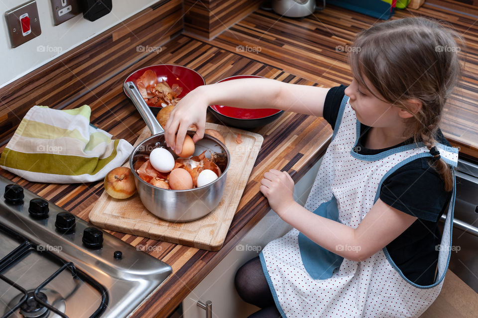 Little girl putting eggs and onion peels together into pot. Easter egg tradition.