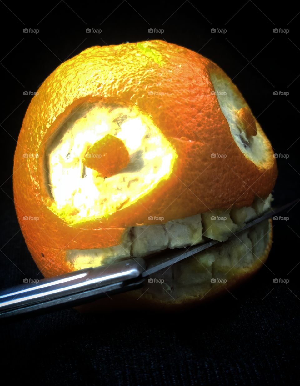 Humor.  Evil orange face with a folding metal knife in its mouth