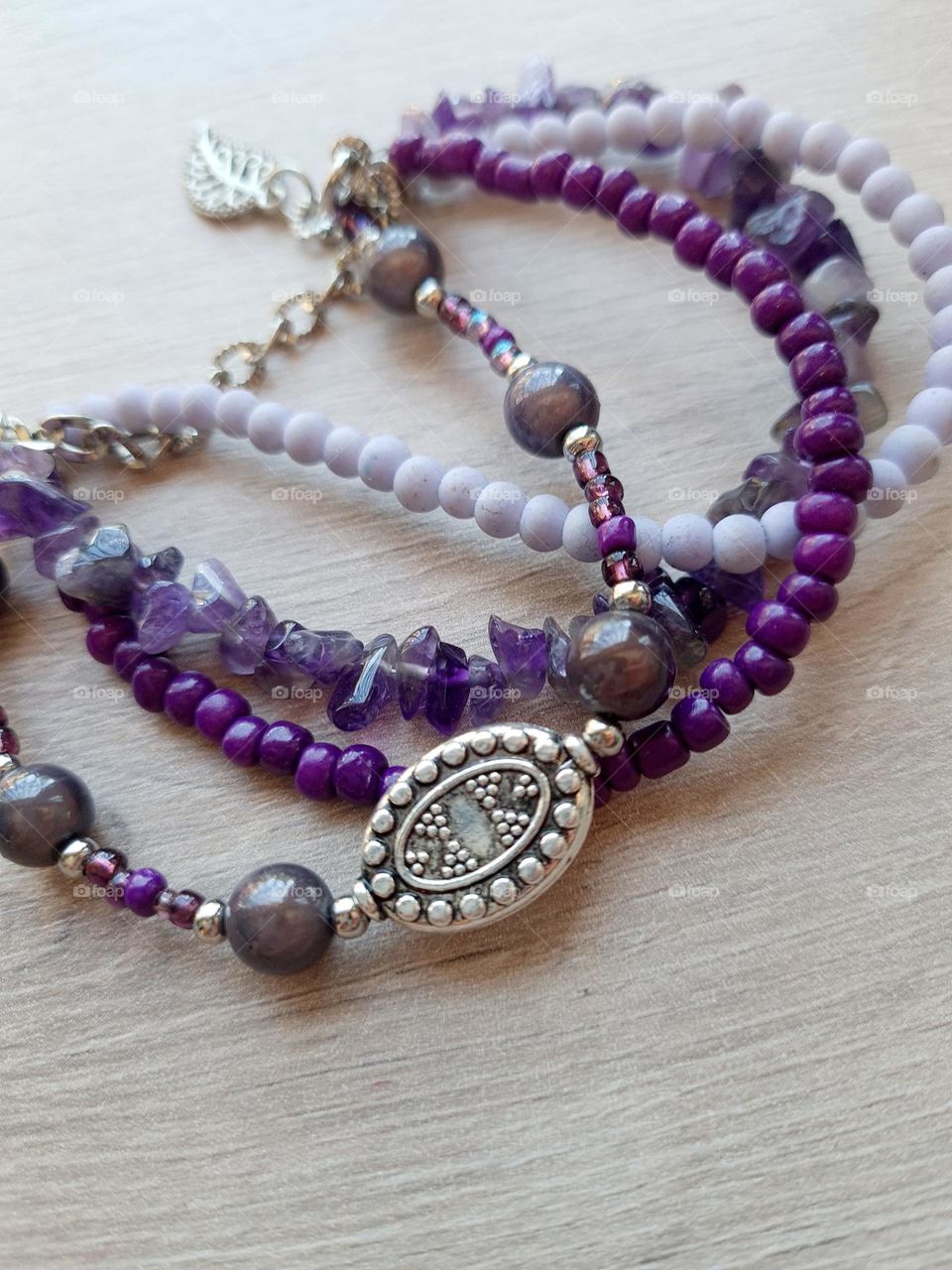 bracelet made from different shades of purple and lilac glass and Stine beads, with silver medal charm on top of a wooden surface