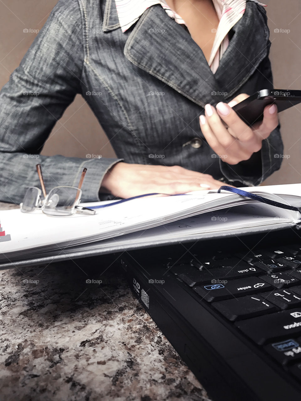 Young business woman using mobile phone and a laptop while checking her planner at the work space 