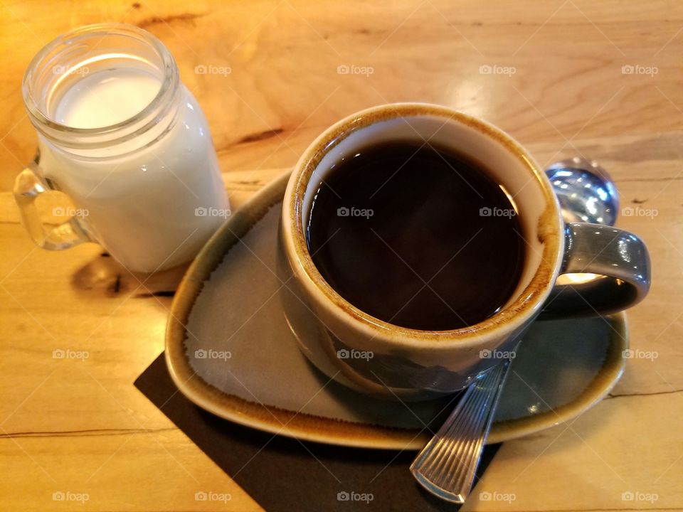 A mug of coffee on a saucer with a mini cup of creamer and a spoon