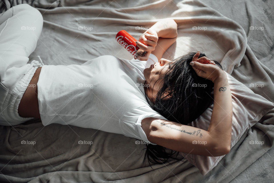 the girl lies on the bed and holds a Coca Cola