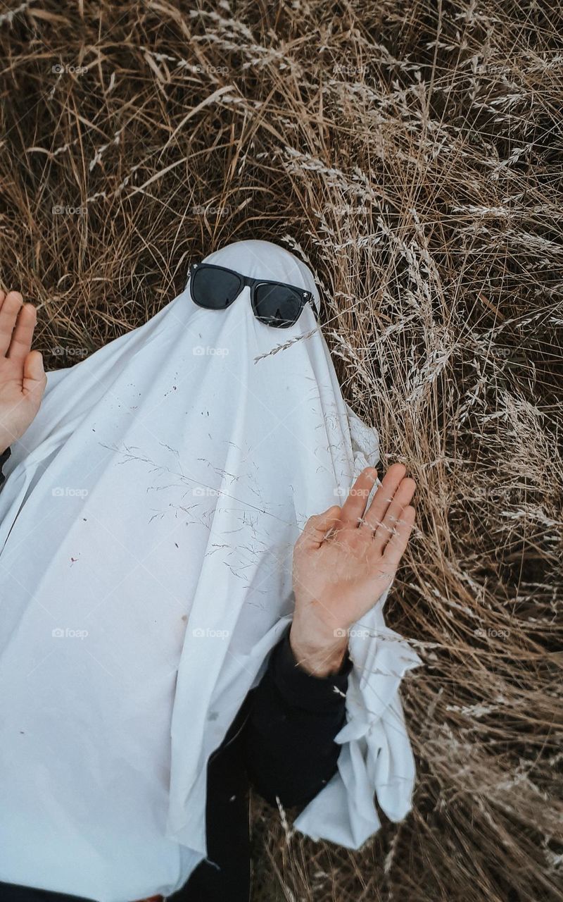 a man in a ghost costume lies among the dry autumn grass