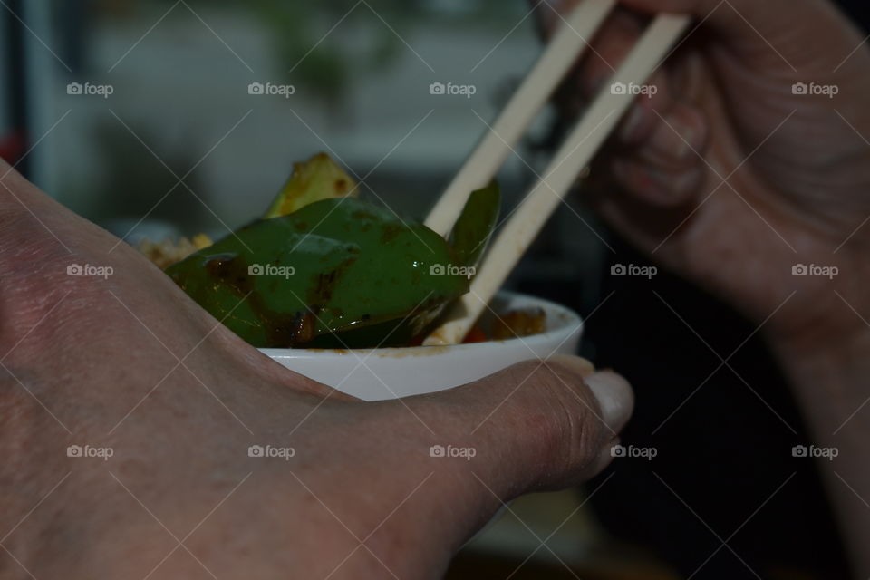 Man using chopsticks eating stir fry vegetables from bowl, close to mouth, Asian cuisine 