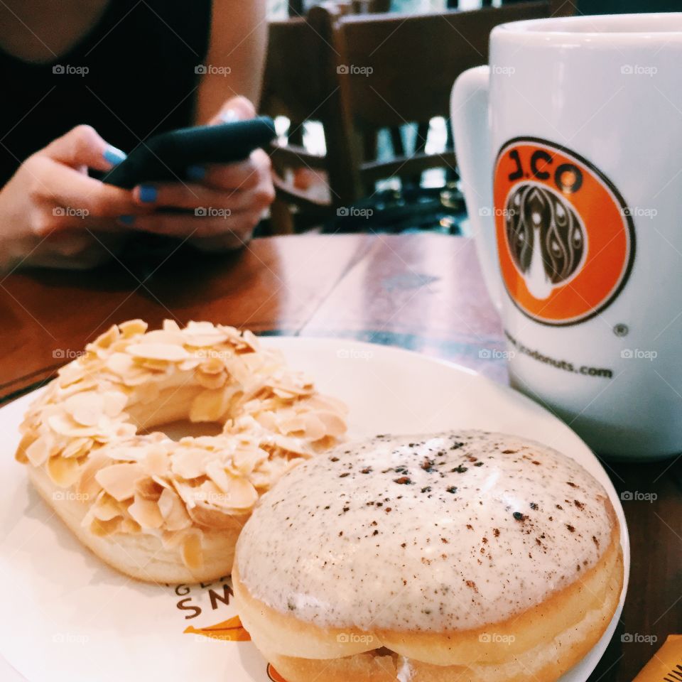 Having donuts and coffee during a rainy afternoon using a smart phone 