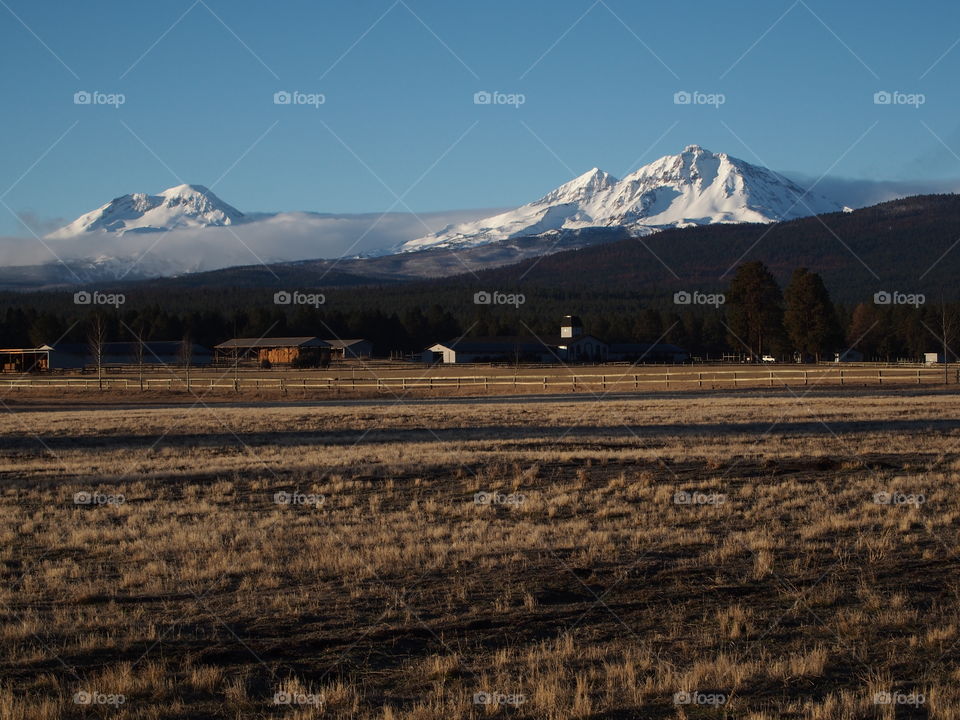 The majestic snow covered Three Sisters in Central Oregon’s Cascade Mountain Range overlook a farm field during the off-season on a beautiful sunny day. 