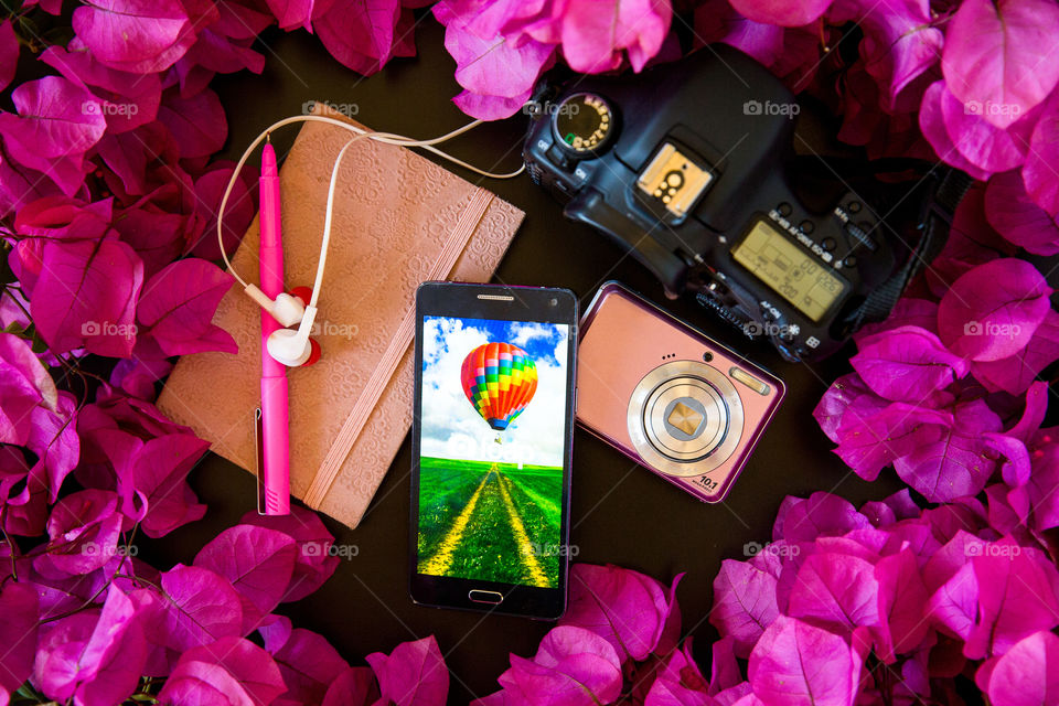 My escape from a tough day is to pick up my camera listen to some music and take photos for foap. Image of camera notebook pen foap on smartphone and pink flowers