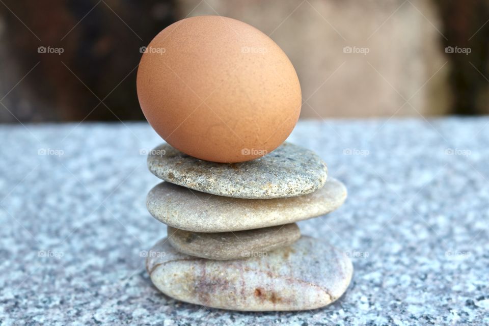 Brown egg balancing atop smooth stone rock stack on marble surface, concept life, business, ideas, creativity endurance or stability