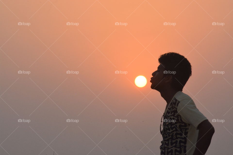 Silhouette of man trying to kissing sun during sunset