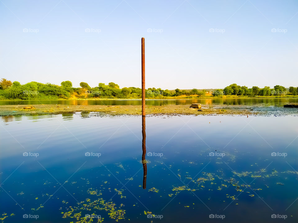 An iron pillar with green trees inside the river water