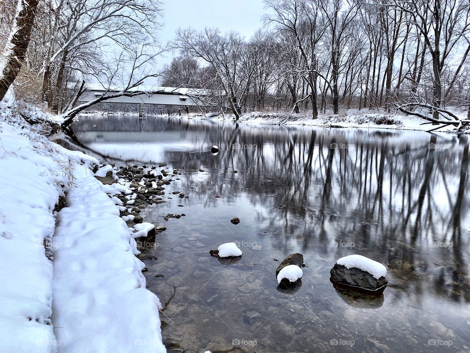 Snowy down down on the white river with the old covered bridge and trees in the background 