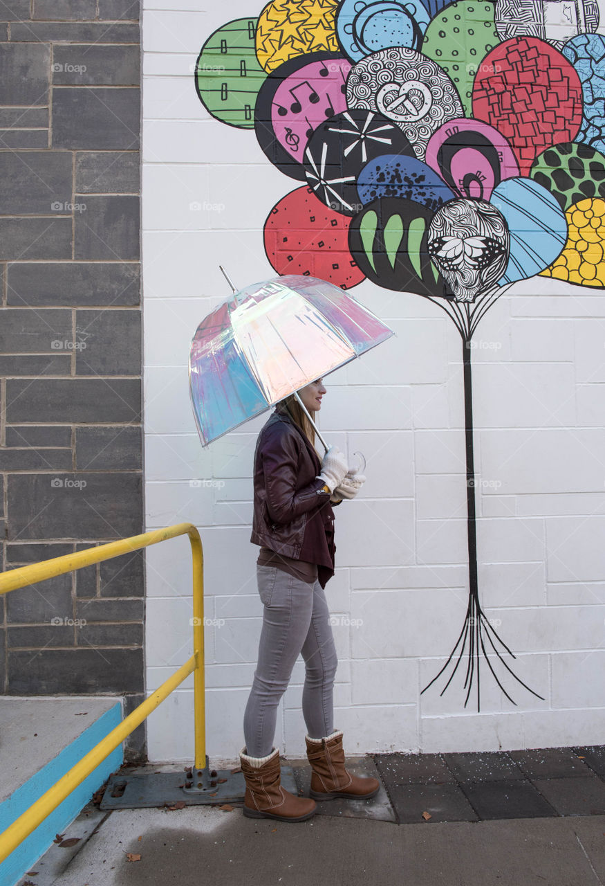 Young woman with an umbrella walking on a sidewalk outdoors in front of a colorful mural