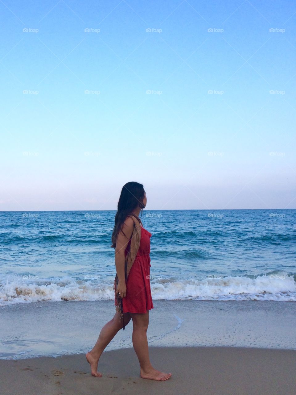 Young woman strolling at the beach, looking to the horizon