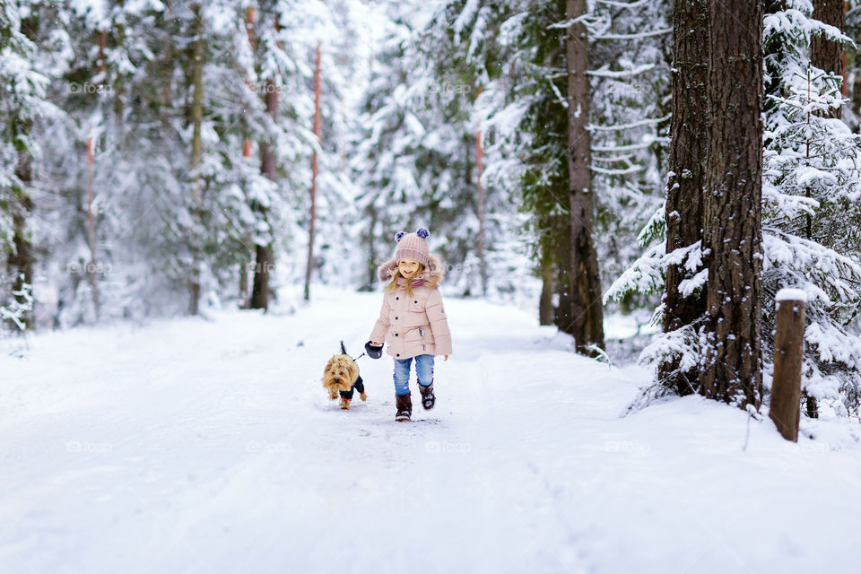 Little girl running in snowy forest with dog 