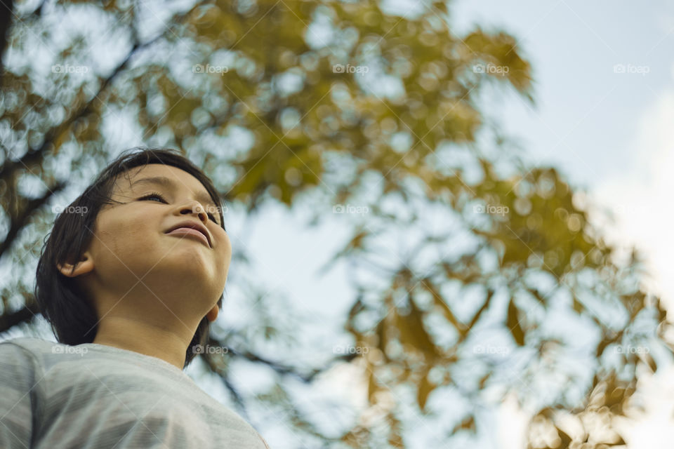 outdoor portrait of happy young eurasian boy on a blurry out of focus bokeh foliage background