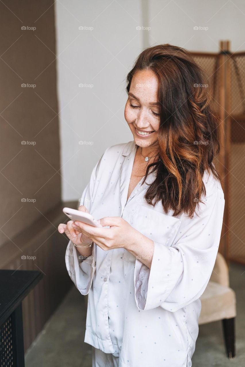 Beautiful woman with long healthy hair using mobile phone at home 