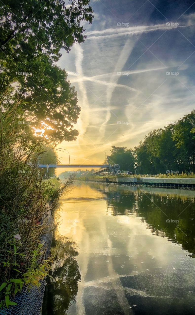 Golden sunrise in the dramatic morning sky, reflected in the water of a river running through a forest.