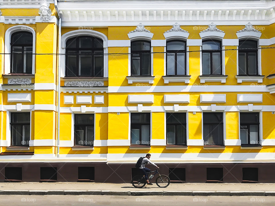 Cyclists riding a bicycle in front of a yellow and white old building in the city 