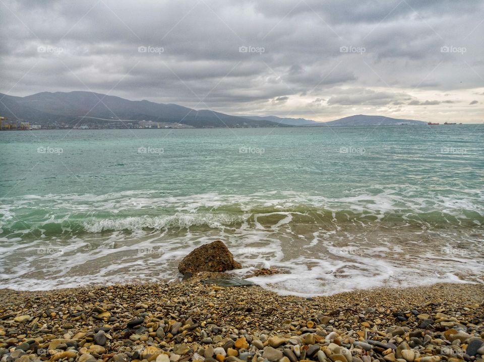 Sea, waves, and heavy rain. Pebble beach. Mountains.