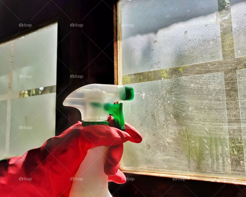 Cleaning the window with a spray bottle and red rubber glove