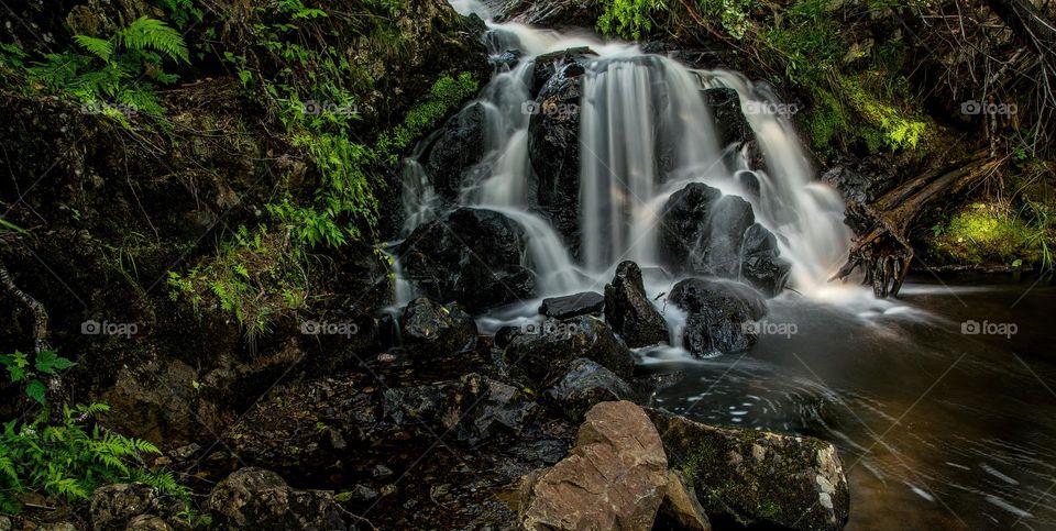 Small waterfalls in forest, with black stones and green leaves, long exposure