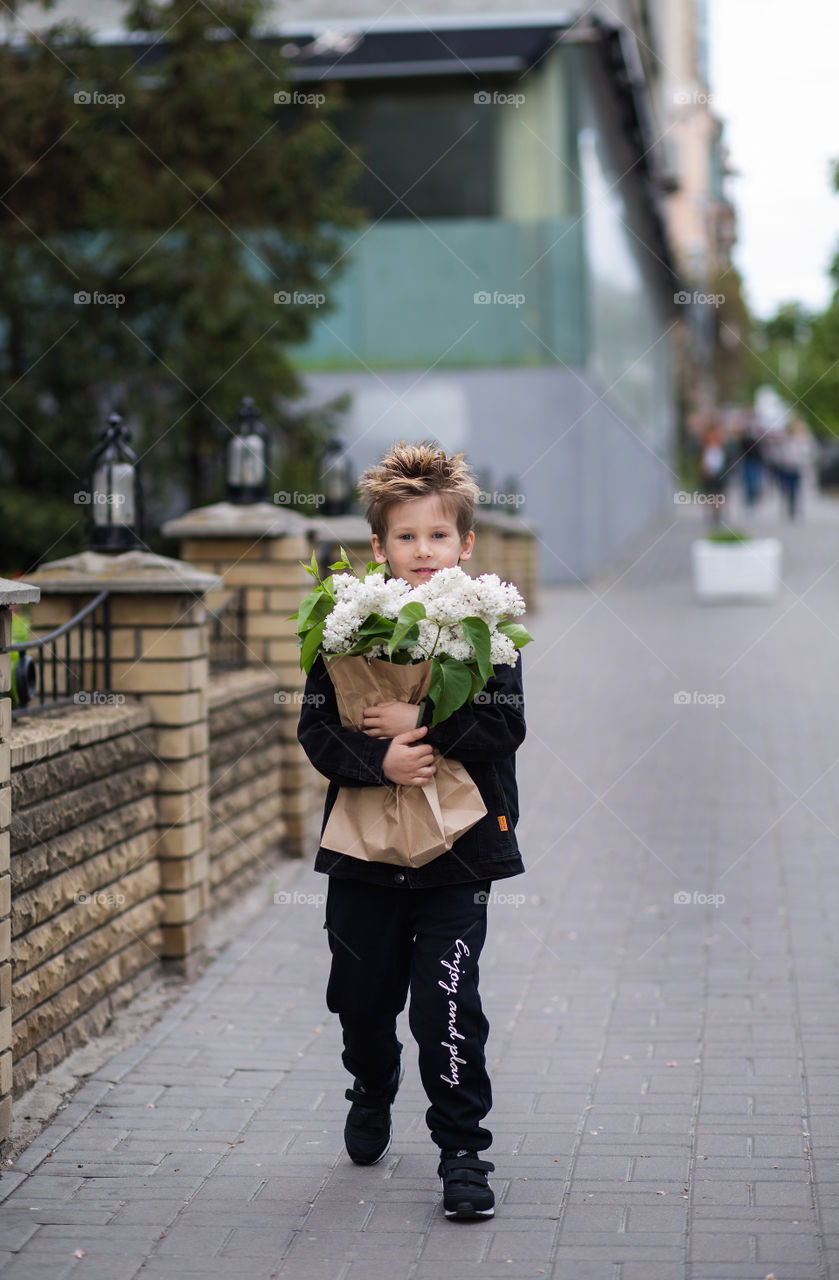 stylish boy in black clothes and glasses is walking along the street.  baby five years old, beautiful blond