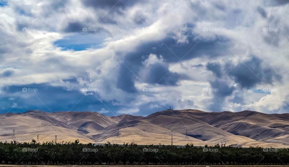 Rolling hills along highway 5 southbound in California with orchards and stunning cloud formations on a beautiful afternoon 