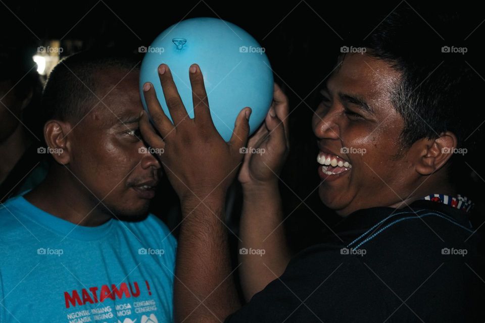 Close up of a group of men looking happy doing a dance game with balloons attached to their heads, a teamwork game to build a great team.