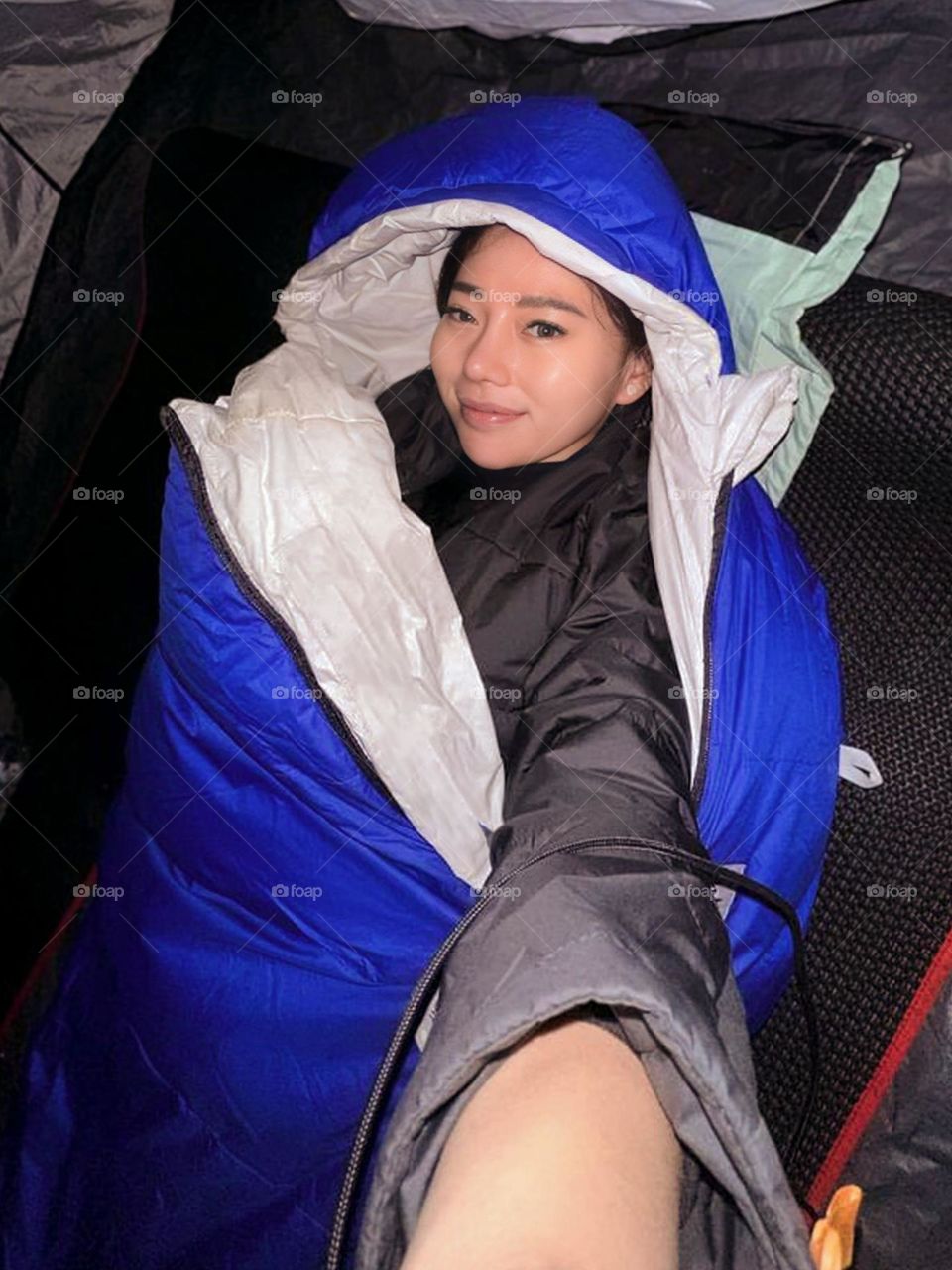 Young woman in a tent with a blue sleeping bag. The person's face appears smiling, and they appear to be in a sleeping or resting state