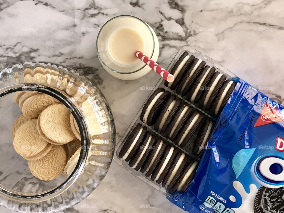 Double stuff Oreo chocolate cookies and golden double stuff Oreo cookies and a glass container of milk with a red and white straw Flatlay